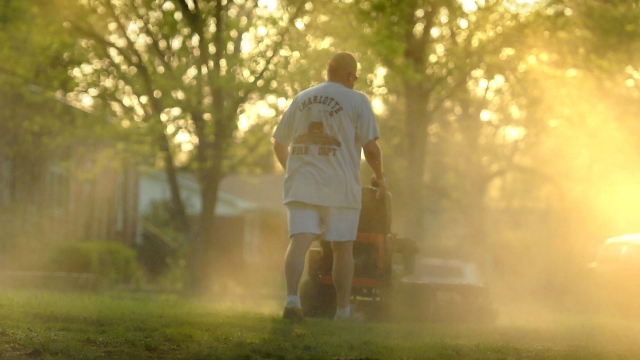 A man kicks up a cloud of pollen as he mows his front yard