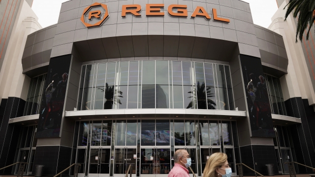 Two shoppers walk past a Regal movie theater.