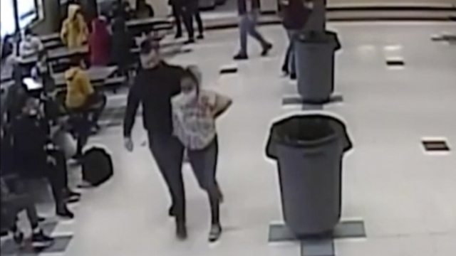 Frame grab from surveillance video shows an off-duty officer escorting a student out of the cafeteria