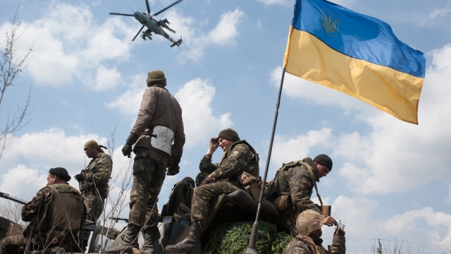 A Ukrainian Army helicopter flies over a column of Ukrainian Army combat vehicles