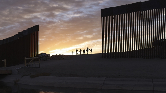 A migrant family passes through a gap in the border wall.