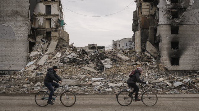 People ride bicycles next to a building destroyed by Russian forces in Ukraine.