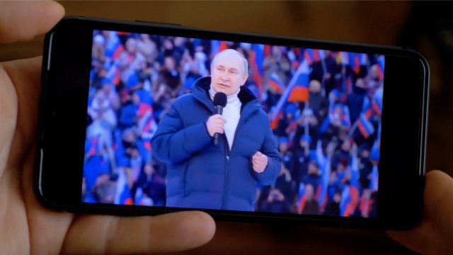 A person holds a phone displaying Russian President Vladimir Putin speaking.