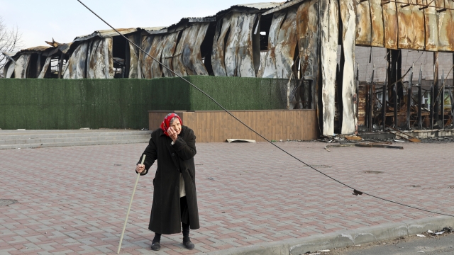 An elderly local resident stands behind a destroyed part of a building in Ukraine