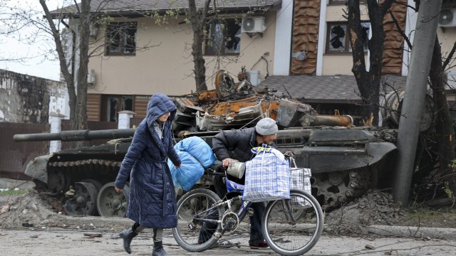 Local civilians walk past a tank destroyed during heavy fighting in Ukraine