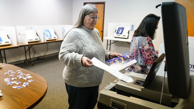 A voter inserts her ballot into a scanner.