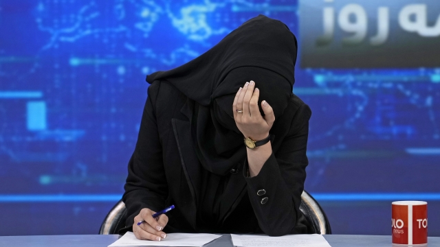 TV anchor Khatereh Ahmadi bows her head while wearing a face covering as she reads the news on TOLO NEWS.