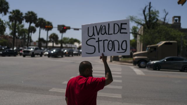 A man holds a sign on a street corner saying "Uvalde Strong."