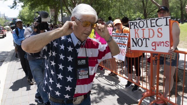 An NRA member plugs his ears as he walks past protesters.