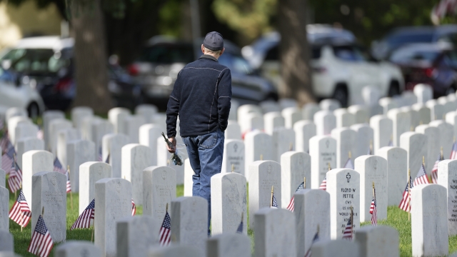 A man carries a bouquet of flowers amid headstones in Fort Logan National Cemetery.