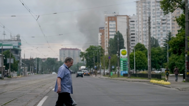 A man crosses a street as smoke rises in the background after Russian missile strikes in Kyiv, Ukraine