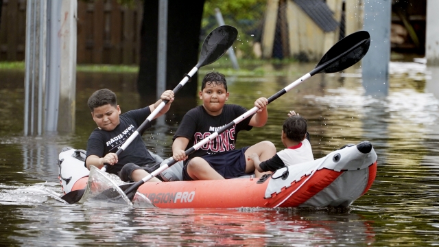 Young boys paddle an inflatable kayak on a flooded Miami street