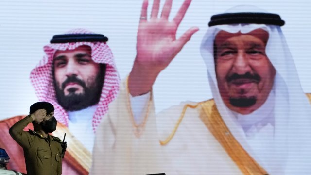 A Saudi policeman salutes in front of a screen displaying images of Saudi King Salman and Crown Prince Mohammed bin Salman.