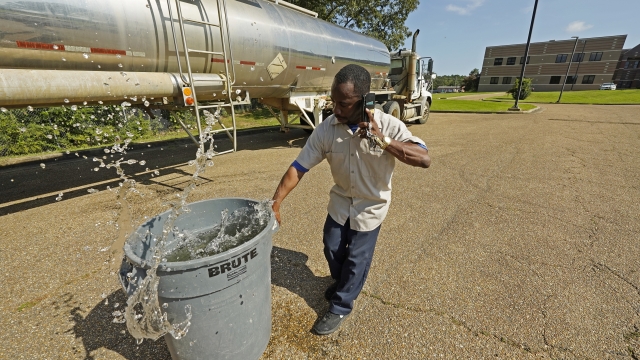 A custodian in Jackson, Miss., hauls away a trash can filled with water from a tanker