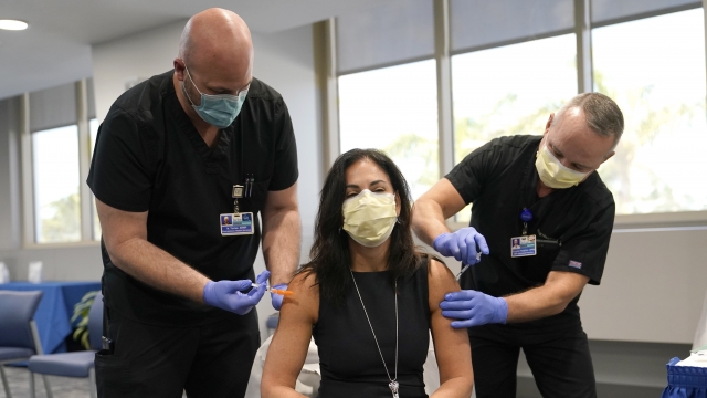 Dr. Lilian Abbo, center, receives a flu vaccine from Nicholas Torres, left, and a Pfizer COVID-19 booster shot