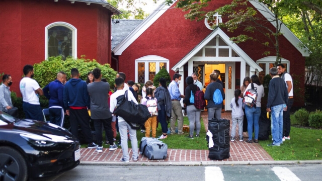 Immigrants gather with their belongings outside of a church