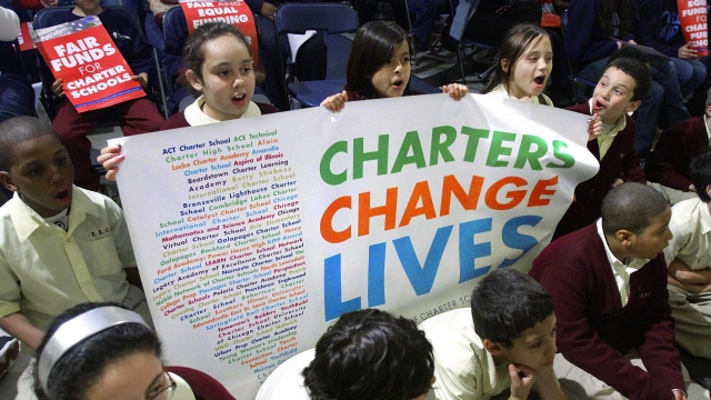Students hold a sign saying, " Charters Change Lives."
