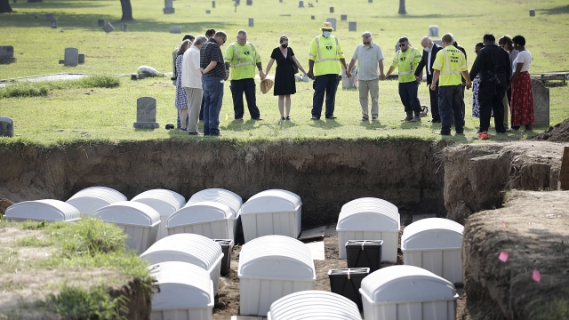 A group prays during a small ceremony as remains from a mass grave are re-interred at Oaklawn Cemetery