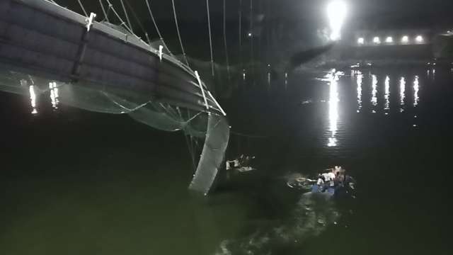 Rescuers on boats search in the Machchu river next to a cable bridge that collapsed in India.