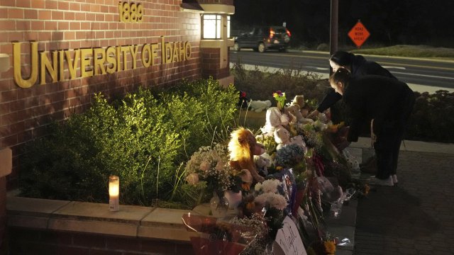 Two people place flowers at a growing memorial in front of a campus entrance sign for the University of Idaho.