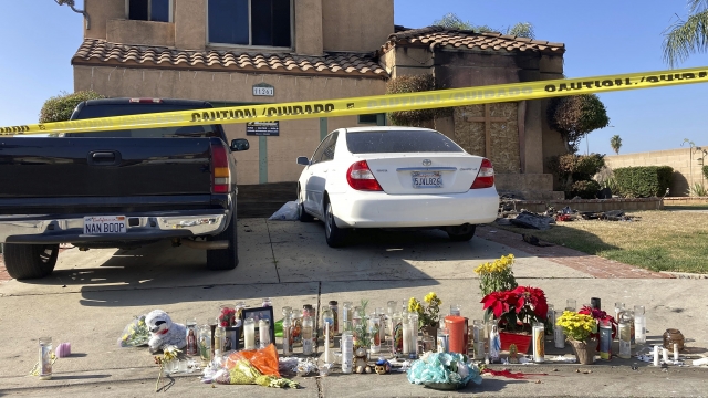 Candles and flowers are displayed outside of the charred home in Riverside, California.