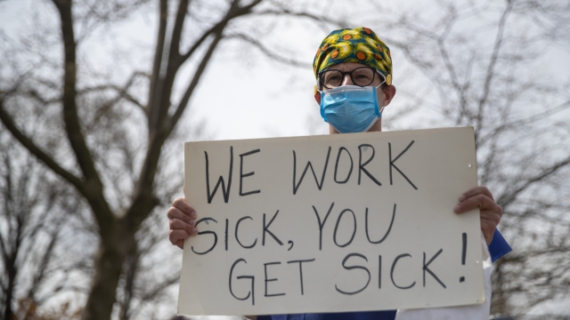 A nurse holds a sign saying, "We work sick, you get sick."