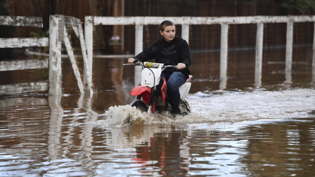 A boy rides his motorcycle around his flooded home.