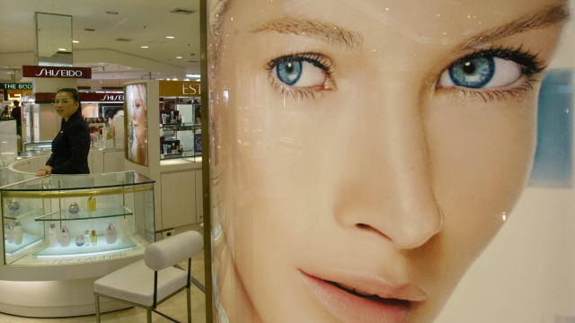 A cosmetics sales clerk is pictured near a large ad for skin whitening cream.