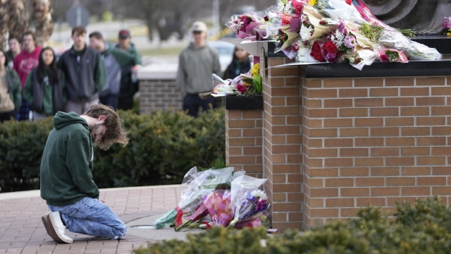 A student kneels where flowers are being left at the Spartan Statue on Michigan State University's campus.