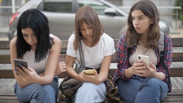 Three girls sit on their phones.