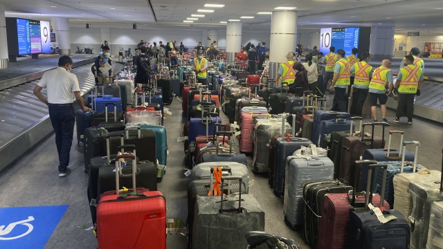 Airport workers arrange rows of suitcases.