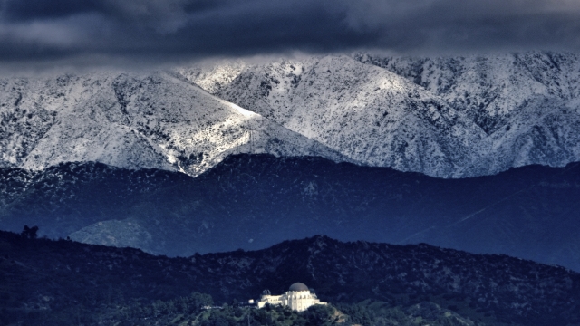 Storm clouds and snow are seen over the San Gabriel mountain range behind Griffith Observatory in the Hollywood Hills