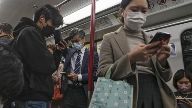 Commuters wearing face masks browse their smartphones as they ride on a subway train in Hong Kong