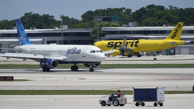 A JetBlue plane passes a Spirit Airlines plane on a runway.