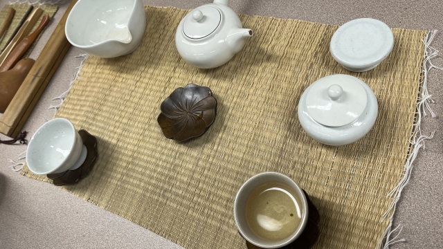 A teapot and cups sit on a woven mat as a tea ceremony is being prepared.
