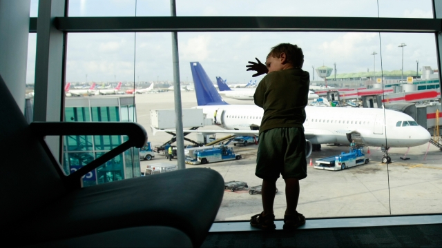 Young boy looks at planes out the window at an airport.