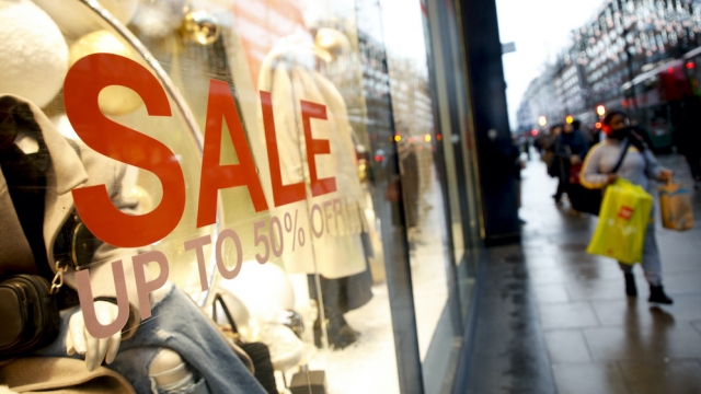 A shopper carries bags past a sale sign in the window of a clothing store.