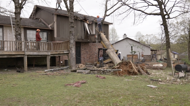 People work on removing a tree that fell into a house