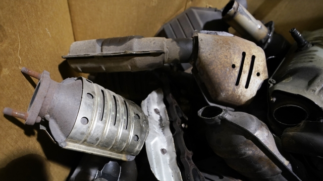 Used catalytic converters that were removed from cars at a salvage yard are piled up in a carton.