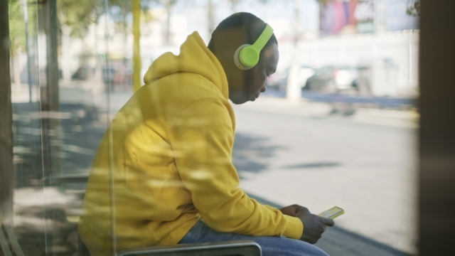 A person listens to music at a bus stop.