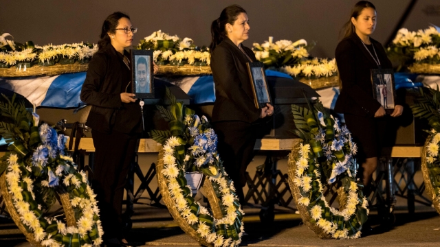 Foreign Ministry officers hold portraits beside the coffins of Guatemalan migrants whose remains arrived in Guatemala City.
