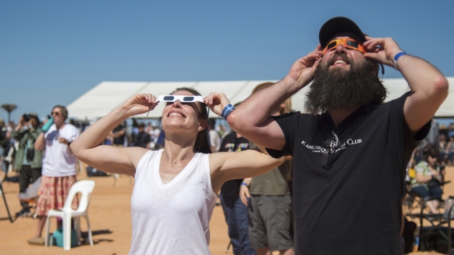 A woman and man use protective glasses to view a solar eclipse.