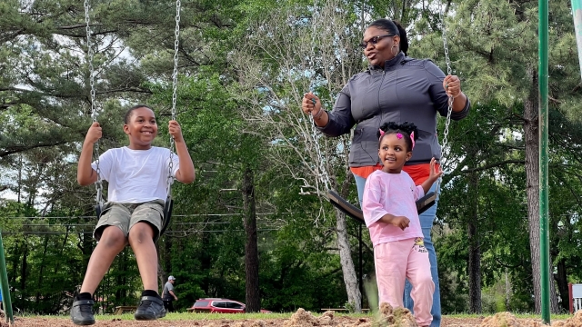 A woman pushes children on a swing set