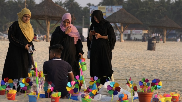 Indian Muslim women wearing hijabs buy toys for their children as they spend an evening at a beach