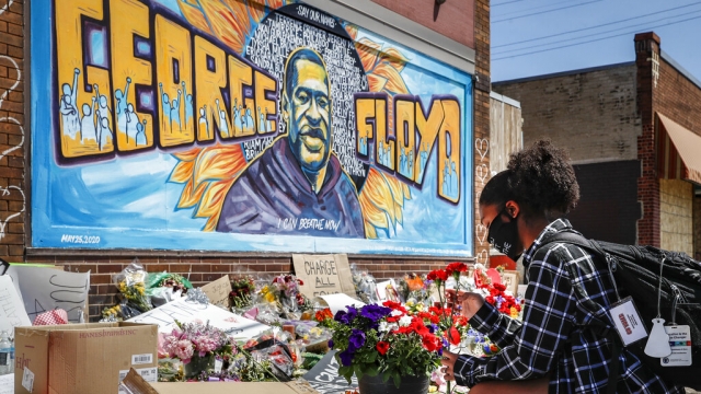 A person places flowers at a memorial mural for George Floyd