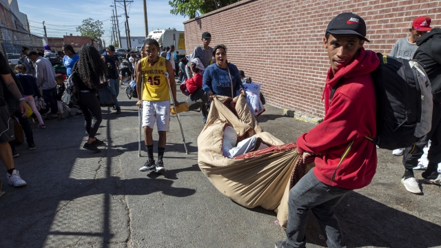Migrants carry their belongings as police officers briefly removed them from an alley to allow the clean up of a camp