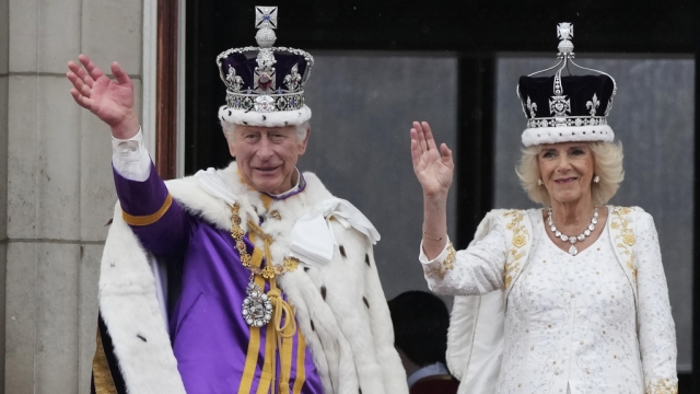 King Charles III and Queen Consort Camilla wave while wearing their crowns.