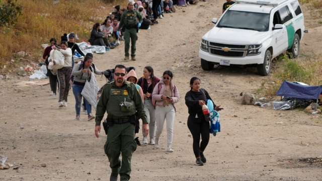 A U.S. Border Patrol agent and a line of migrants.
