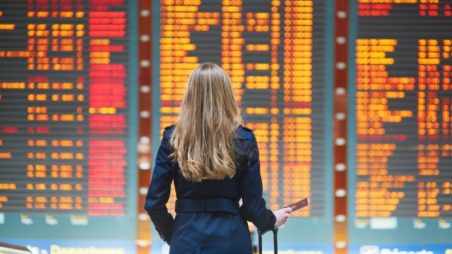Woman looks at a board displaying flight delays.