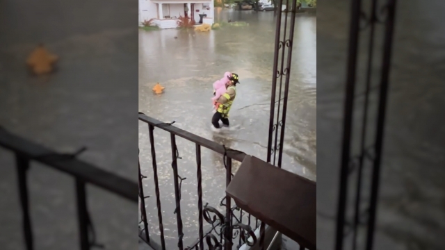 A firefighter carries a child through floodwaters.
